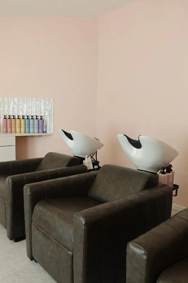 Liberty and Frank salon interior — blush-pink backwash room with two black leather chairs and white basins
