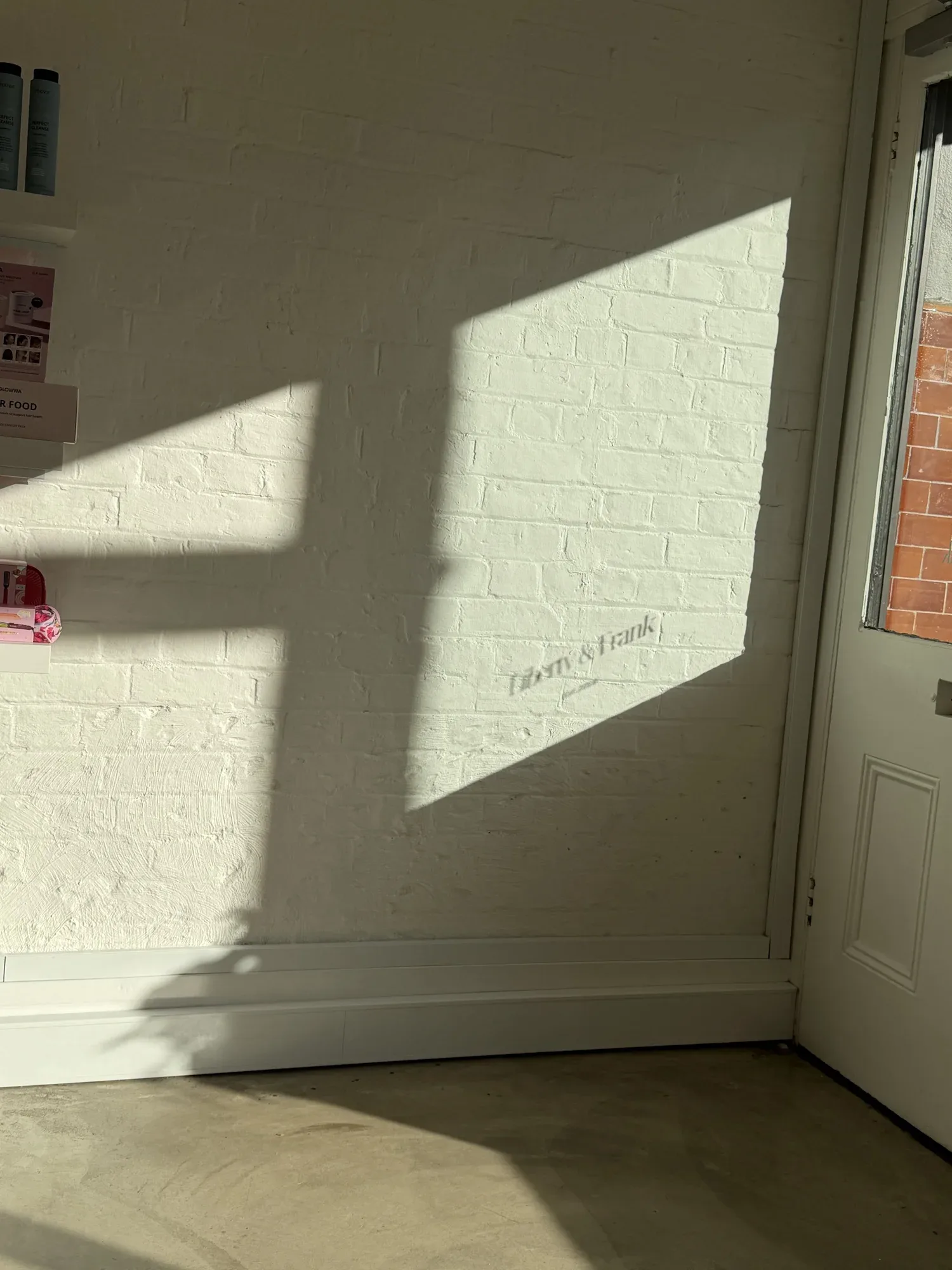 Sunlit white-brick salon interior corner with polished concrete floor and product shelf